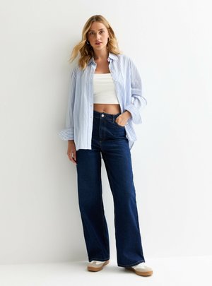 Light blue and white striped button-up shirt, worn over a white cropped top, paired with high-waisted dark denim wide-leg jeans and beige shoes.