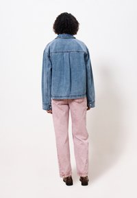 Lichte blauwe spijkerjas, relaxte pasvorm, knopenmanchetten en rugnaaddetail, gecombineerd met roze, hoge taillebroeken en bruine schoenen.