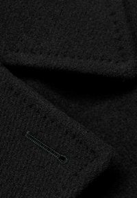 Tessuto di lana nero con una superficie texture, caratterizzato da un accento cucito nello stesso colore del filo. La composizione mette in risalto un materiale morbido e durevole.