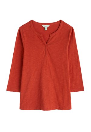 Top de manga larga en color óxido, fabricado con una tela suave, que cuenta con un escote en V y una tapeta con tres botones. Textura suave con un corte relajado.