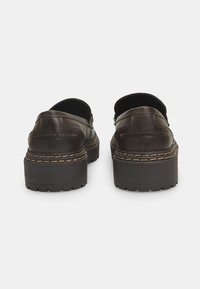 Brūni ādas slip-on apavi ar masīvu melnu platformu un kontrastējošiem diegiem. Apaļa aizmugure ar gludu tekstūru un minimālu noformējumu.