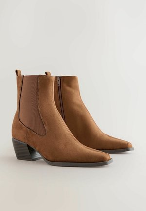Braune Wildleder-Ankle Boots mit spitz zulaufender Zehenpartie, elastischen Seiteneinsätzen und einem niedrigen Blockabsatz. Verfügt über einen Reißverschluss an einer Seite.
