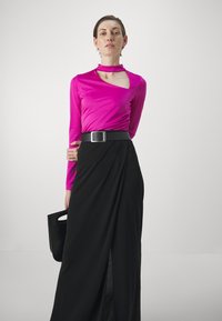 Maglietta a maniche lunghe fucsia con scollatura ampia e dettagli arricciati, abbinata a una gonna nera a portafoglio, completata da una borsa nera.