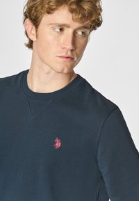 Felpa navy in cotone, con collo rotondo e un piccolo logo ricamato rosa sul lato sinistro del petto, dalla texture morbida.