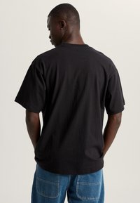 Camiseta de algodón negra con un corte relajado, mangas cortas y cuello redondo. La parte posterior presenta una textura simple y suave sin gráficos ni adornos.