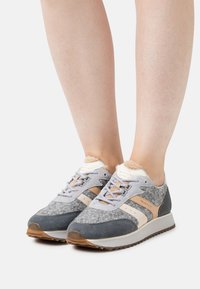 Grey and blue sports shoes made of felt and suede. Features textured accents, beige detailing, and perforated side stripes. Rubber sole.