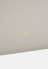 Produit en cuir gris avec un logo doré "FURLA" ; texture lisse avec des coutures soignées le long des bords.