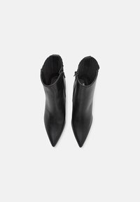 Bottes noires en cuir montant à la cheville avec un bout pointu, une texture lisse et des fermetures éclair latérales. Les côtés présentent des accents côtelés verticaux pour plus de détails.