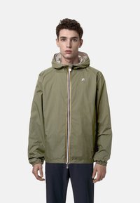 Giacca a cappuccio verde oliva con zip frontale, polsini elasticizzati e una leggera fodera interna. Presenta un piccolo logo sul petto.