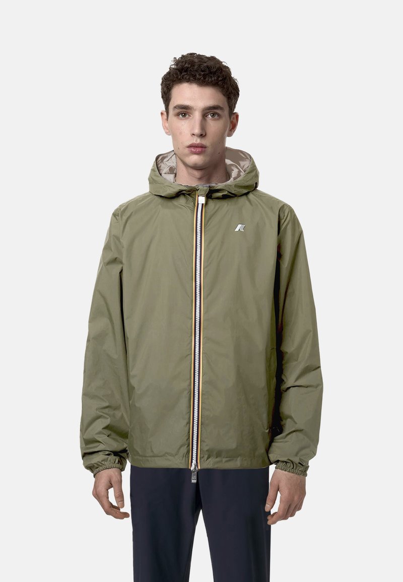Giacca a cappuccio verde oliva con zip frontale, polsini elasticizzati e una leggera fodera interna. Presenta un piccolo logo sul petto.