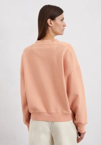 Licht perzik oversized sweatshirt met een ronde halslijn, verlaagde schouders en geribde zoom. Soepele textuur, minimale details aan de achterkant.