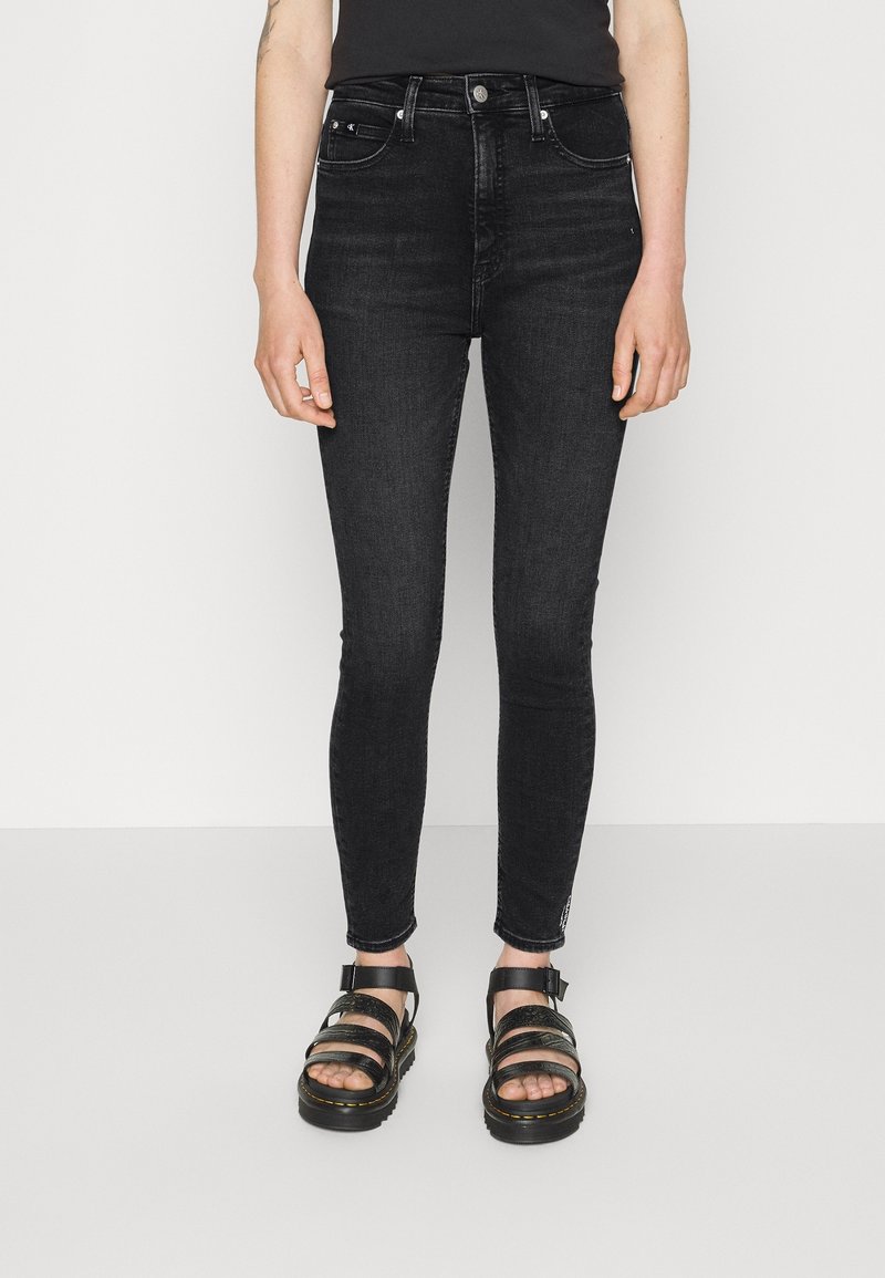 Jeans skinny de tiro alto en denim negro, con un clásico diseño de cinco bolsillos y un aspecto ligeramente descolorido. Combinados con sandalias negras.
