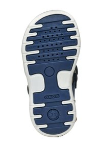 Svršek tenisky s modrou gumovou podrážkou a bílými akcenty, textura pro lepší přilnavost, s vyraženým brandingem a detaily odpružení.