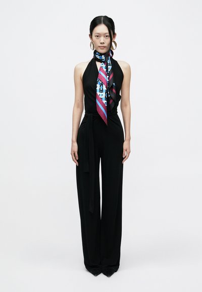 Μαύρη ολόσωμη φόρμα με halter neck, διακοσμημένη με ένα πολύχρωμο φουλάρι με σχέδια δεμένο στο λαιμό. Γυαλιστερά, μεγάλα κρίκοι σκουλαρίκια συμπληρώνουν την εμφάνιση.