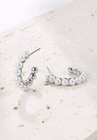 Boucles d'oreilles en argent en forme de créoles, présentant un design de perles brillantes et de perles alternées, avec une surface lisse et une forme courbée.