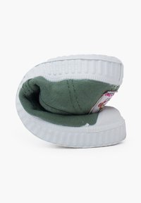 Botte slip-on en toile verte avec une semelle en caoutchouc blanche, présentant des bords arrondis et une couture visible. L'intérieur est en tissu vert avec un petit détail de logo.