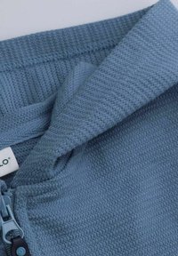 Niebieska teksturowana tkanina z gładkim zapięciem na zamek. Materiał ma tkany wzór i subtelne detale stębnowania. Widoczna etykieta.