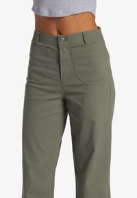 Olijfgroene broek met een rechte pijp, voorzien van twee voorzakken, een knoopsluiting en zichtbare stiksels op de tailleband.
