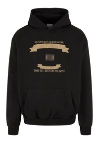 Black hooded sweatshirt featuring gold printed text and a logo patch, ribbed cuffs and hem, and a front kangaroo pocket.