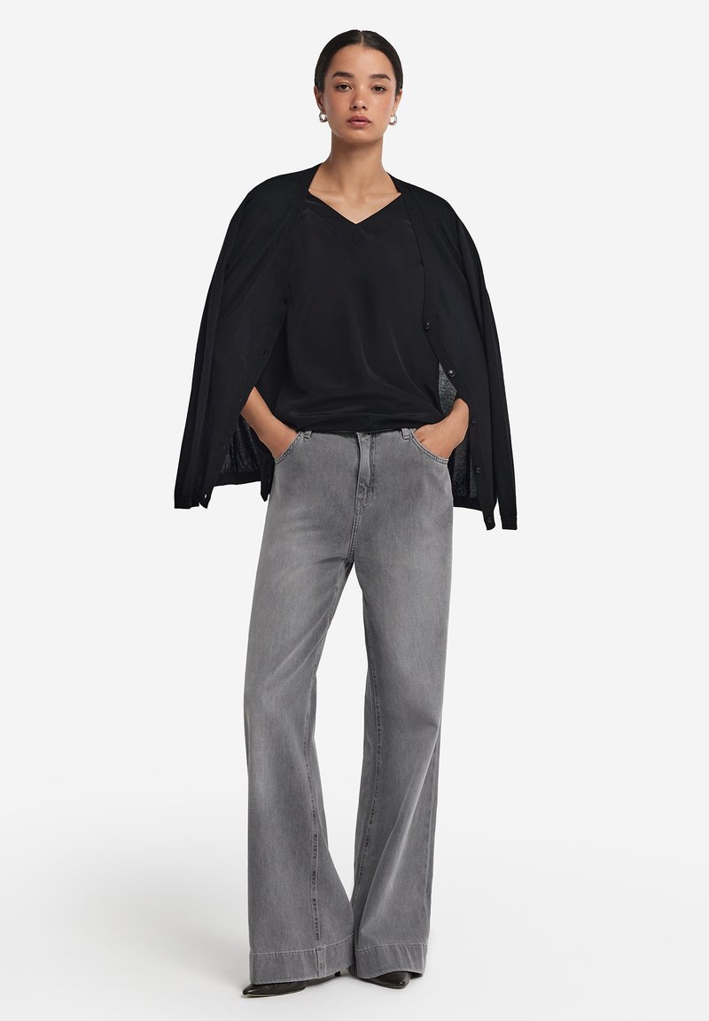 Cardigan nero a maniche lunghe sopra un top nero a V, abbinato a jeans grigi a gamba larga e in vita alta. Design semplice con una texture liscia.