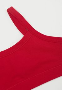 Červená sportovní podprsenka z bavlněné směsi s tenkými ramínky a bezešvým designem. Materiál má hladkou texturu a minimální švy.