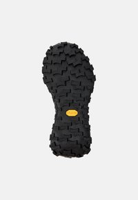 Černá gumová podešev s vícesměrným vzorkem a logem Vibram; obsahuje vyvýšené bloky pro lepší přilnavost a stabilitu.