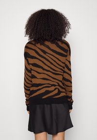 Maglione a righe marrone e nero con una texture a maglia liscia. Il design presenta un audace motivo a strisce di tigre con un orlo nero.
