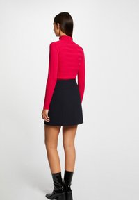 Suéter rojo ajustado de cuello alto con rayas verticales, combinado con una falda negra en línea A. Botas negras brillantes hasta la rodilla completan el look.