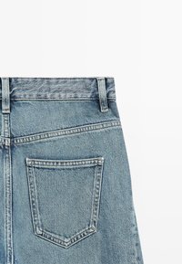 Jasnoniebieskie dżinsy z denimu z wysokim stanem, z tylną kieszenią i widocznym przeszyciem wzdłuż pasa i szwów.