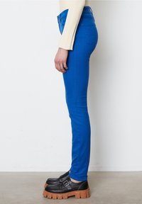 Jeans ajustados azules confeccionados en tela elástica, con una cintura alta, diseño de cinco bolsillos y una textura suave, combinados con zapatos negros gruesos.