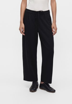 Person wearing black wide-leg pants with drawstring waist and black lace-up shoes standing on a plain white background.