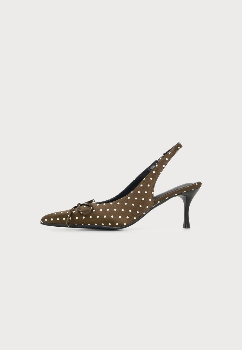 Chaussure à talon haut slingback marron à pois blancs, bout pointu, petit nœud et talon stiletto noir sur fond uni.