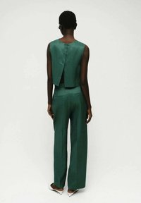 Grünes Zweiteiler-Outfit mit einem ärmellosen Top mit Knopfdetails auf der Rückseite und weiten Hosen, beide aus einem glatten, matten Stoff.