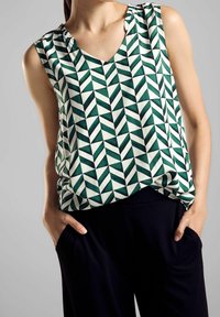 Ärmlös topp i grön och vit med geometriskt mönster. V-ringad design med subtila rynkor vid axeln. Matchad med mörka, löst sittande byxor.