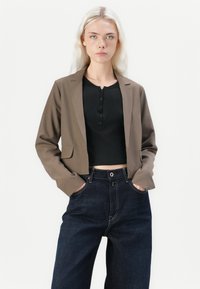 Brun cropped blazer med en jevn tekstur, kombinert med en svart ribbestrikket topp og høy midje mørk denimbukser, med frontlommer og søm detaljer.