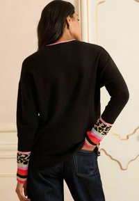Črn oversized pulover z dolgimi rokavi, ki ima pisane črte in leopardji vzorec na manšetah. Mehka pletenina, sproščen dizajn.