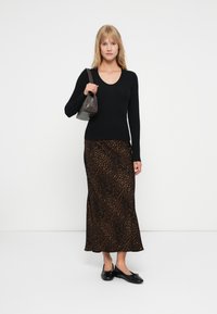 Sort langærmet ribbet top parret med en brun leopardmønstret maxiskirt. Modellen holder en lille grå håndtaske og har sorte flade sko på.
