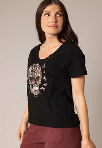 Black cotton T-shirt with a V-neck design featuring a floral skull graphic in vibrant colors and butterfly accents. Short sleeves.