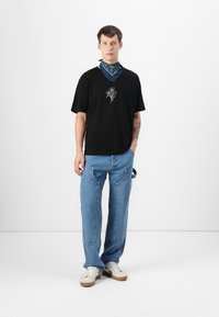 Sort kortærmet T-shirt med broderet rosedesign, parret med lyseblå løse jeans og et blåt bandana om halsen. Hvide sneakers.