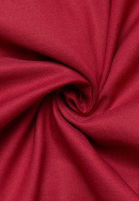 Tessuto intrecciato e testurizzato di un ricco rosso, con una trama fitta e una finitura morbida, disposto in una formazione a spirale che mette in evidenza il suo movimento.