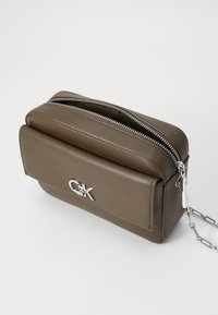 Borsa a tracolla in pelle sintetica marrone con chiusura a zip argentata, tasca frontale e tracolla a catena; presenta un'accenno di logo metallico.