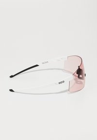 Lunettes de soleil avec une grande lentille rose, monture blanche avec des accents noirs, présentant un design épuré et un logo minimaliste.
