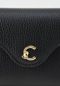 Primo piano di una pattina di un portafoglio in pelle nera texture con una chiusura dorata curvata a forma di lettera C stilizzata.