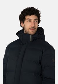 Marineblauwe donsjas met een hoge kraag en een capuchon. Horizontale doorgestikte design en een logopatch op de linker mouw. Gestructureerde stof.