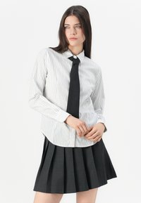 White striped button-up shirt with a collar, paired with a black tie and a pleated black skirt, featuring textured fabric and defined lines.