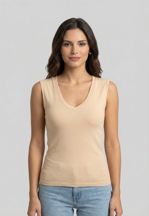 Donna con lunghi capelli castani che indossa un top beige senza maniche con scollo a V e jeans azzurri chiari su uno sfondo grigio uniforme.