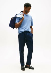 T-shirt azzurro chiaro a girocollo, pantaloni navy con cordoncino e mocassini neri. Una grande borsa tote navy con spalline bianche è appoggiata su una spalla.
