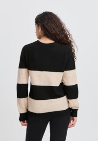 Jersey de punto con rayas horizontales en negro y beige, cuello redondo, mangas largas y puños acanalados. Textura suave y ajuste relajado.