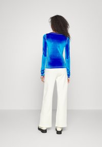 Långärmad ljusblå sammetstop med en figurnära design, parat med högmidjade vita vida byxor och svarta kängor med tjock sula.