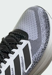 Chaussures de sport avec un dessus en maille gris et noir, des accents en plastique et une semelle texturée avec un logo à trois bandes proéminent en blanc.